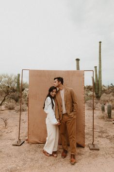 a man and woman standing next to each other in front of a desert backdrop with cacti