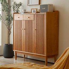 a wooden cabinet sitting next to a plant in a living room on top of a hard wood floor