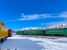 two green and red trains traveling down train tracks in snow covered countryside with mountains in the background