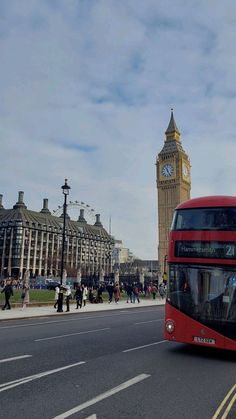 a red double decker bus driving down a street next to tall buildings and a clock tower