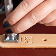 a person is stamping the letter w on a piece of leather with a nail file