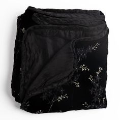 three black bedspreads with white flowers on them, one is folded and the other has