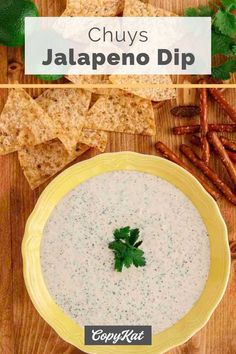 a bowl filled with white sauce next to some crackers and cilantros