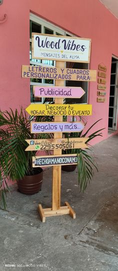 a wooden sign with many different signs on it in front of a pink wall and potted plant