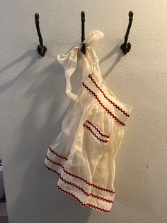 a white dress hanging on the wall next to two black coat hooks with red and white trim