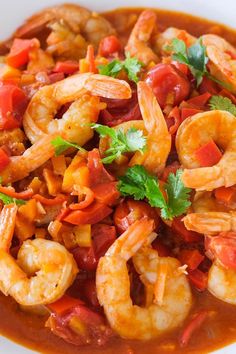 a white bowl filled with shrimp and tomato soup, garnished with cilantro