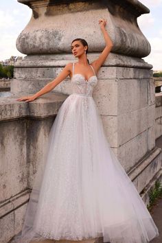 a woman in a white dress leaning against a stone wall