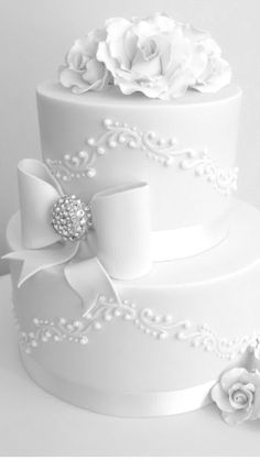 a three tiered white wedding cake decorated with flowers and pearls, on a table