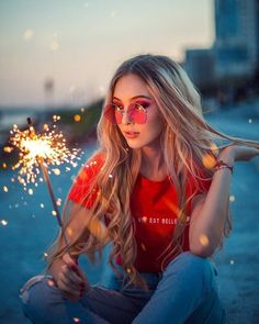 a young woman sitting on the ground holding a sparkler in her hand and looking at the camera