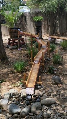 a wooden walkway in the middle of a garden with rocks and plants around it,