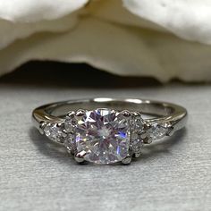 an engagement ring with three stones on it and a white rose in the background,