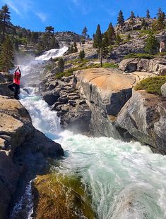 a man standing on the edge of a cliff next to a river with water running down it