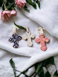 three cross shaped brooches sitting on top of a white cloth next to flowers