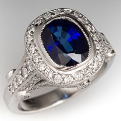 This glimmering ring is centered with one (1) bezel set cushion cut sapphire that is bordered by twenty-one (21) bead set round brilliant cut diamonds. The shoulder and side faces of the ring are set with sixty-eight (68) bead set round brilliant cut diamonds, and six (6) bezel set round brilliant cut diamonds. The ring has milgrain edging.  It measures 12.9mm at the top, rises 7.1mm above the finger, and tapers to 2.5mm wide by 1.5mm thick at the base of the shank. There are a few very light sw Luxury Gia Certified Cushion Cut Sapphire Ring, Formal Cushion Cut Lab-created Sapphire Ring, Luxury Sapphire Ring Cushion Cut Brilliant, Luxury Sapphire Ring With Cushion Brilliant Cut, Luxury Cushion Cut Sapphire Ring With Brilliant Cut, Luxury Sapphire Ring With Cushion Cut Center Stone, Luxury Cushion Cut Sapphire Ring With Center Stone, Elegant Cushion Cut Sapphire Ring With Diamond, Formal Sapphire Halo Ring Cushion Cut