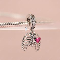 This is charm only, bracelet is sold separately. Experience true love with this exquisite pendant charm featuring a silver rib cage adorned with a stunning pink heart stone. Made of high-quality 925 sterling silver, its polished finish adds a brilliant shine and is accented with a platinum plating. Add this beautiful love oath of rib dangle pendant charm to your bracelet or gift it to your special someone. Materials: 925 sterling silver, cubic zirconiaFinish: platinum plateDimensions: 0.76 x 0.4 Sterling Silver Heart Charm Pendant, Sterling Silver Heart Charm Round Pendant, Pink Sterling Silver Charm Necklaces, Pink Sterling Silver Charm Necklace, Pink Sterling Silver Charm Necklaces With Lobster Clasp, Nickel-free Pink Sterling Silver Charm Necklaces, Pink Sterling Silver Charm Necklace With Heart Charm, Sterling Silver Charm Necklace With Lobster Clasp In Pink, Pink Sterling Silver Necklace With Heart Charm