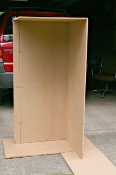 an open cardboard box sitting on the ground next to a red car in a garage