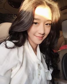 a woman sitting in the back seat of a car with long black hair and wearing a white shirt