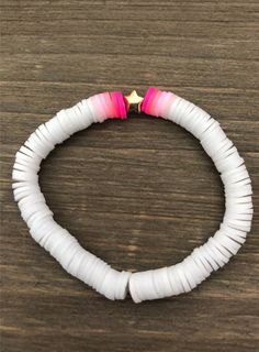 a white bracelet with pink and gold beads on top of a wooden table next to a star