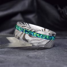 a silver ring with blue and green stones in it next to a knife on a black cloth