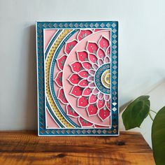 a pink and blue card sitting on top of a wooden table next to a potted plant