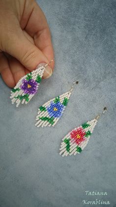 a hand is holding some beaded earrings in front of the earring, which has flowers on it