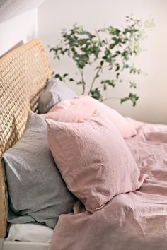 a bed with pink sheets and pillows next to a potted plant