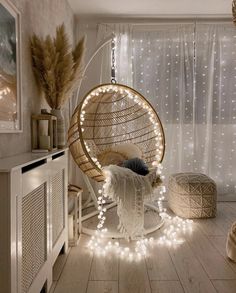 a hanging chair with lights around it in a room that has white curtains and wooden floors