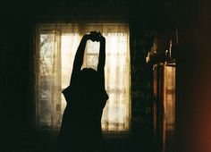 a woman standing in front of a window holding her hands up to the light coming through