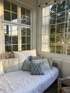 a white day bed sitting in front of two windows with pillows on top of it