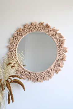 a round mirror hanging on the wall next to a plant and dried flowers in a vase