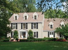 a large gray house with black shutters and white trim on the windows is surrounded by lush green grass