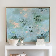 an abstract painting hangs on the wall above a white shelf with two bowls and a basket