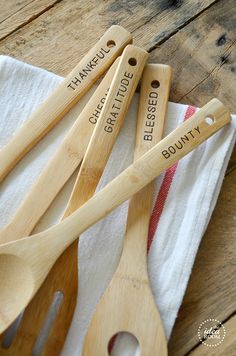 four wooden spoons with engraved names are sitting on a white dish towel next to two forks