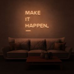 a couch sitting in front of a neon sign that says make it happen on the wall