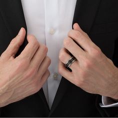 a man in a tuxedo is adjusting his ring on his finger and wearing a black suit