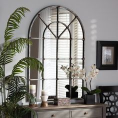 a mirror and some flowers on a table in front of a window with shutters