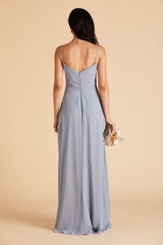 the back of a woman wearing a blue dress with spaghetti straps and flowers in her hand