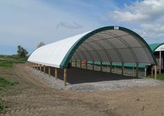 a large white tent sitting on top of a dirt field next to a green and white building