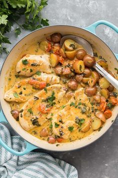 a pot filled with chicken and potatoes on top of a blue towel next to parsley