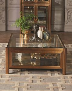 a coffee table with a glass top and gold trim around the edges, in front of a mirrored cabinet