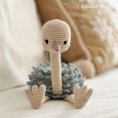 a crocheted bird sitting on top of a bed next to a pillow and pillows