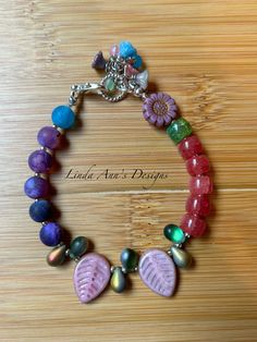 a colorful bracelet with shells and flowers on it, sitting on top of a wooden table