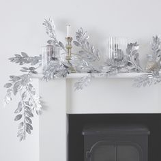 a white fireplace with silver leaves and candles