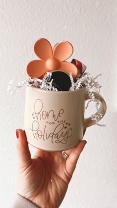 a woman holding a coffee mug with some decorations in it and the words home is holiday written on it