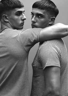 two young men standing next to each other in front of a wall with their arms around one another