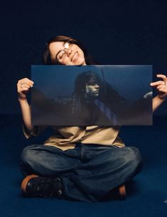 a woman sitting on the floor holding up a poster