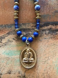 I hand crafted this one-of-a-kind necklace with a Buddhist amulet pendant, and blue natural stone, glass, and gold tone metallic beads.  The pendant is a Buddhist amulet from Thailand, depicting a revered Thai Buddhist monk on the front and a message in Thai on the back.  This amulet has been blessed by a Thai Buddhist monk.  The necklace measures 22 inches long, with an additional 1.25 inches for the pendant.  It has a toggle clasp. Ours is a non-smoking home. Future Jewelry, Amulet Necklace, Natural Stone Beads, Buddhist Monk, Gold Hand, Gold Hands, Toggle Clasp, Blue And Gold, Hand Beading