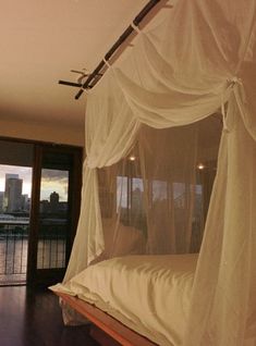 a canopy bed with white drapes over it in a bedroom next to a large window