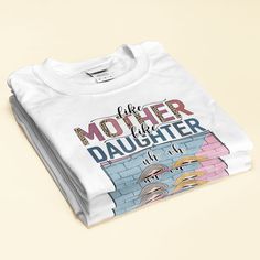 a white t - shirt with the words mother and daughter printed on it, sitting against a beige background