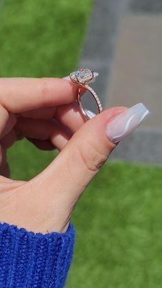 a woman's hand holding a diamond ring on top of her finger, with grass in the background